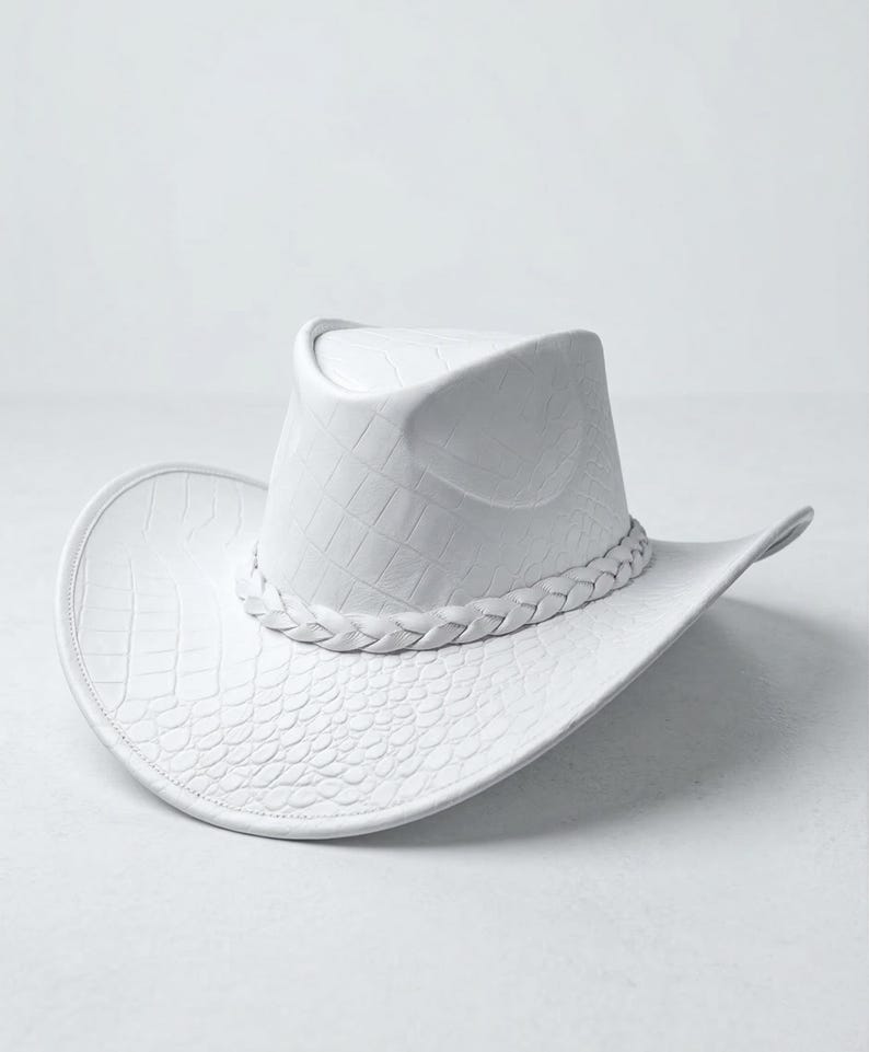 May include: A white cowboy hat with a textured, crocodile-like pattern. The hat features a braided band around the crown and a wide brim. The hat's dimensions are approximately 15 inches in length and 12 inches in width.