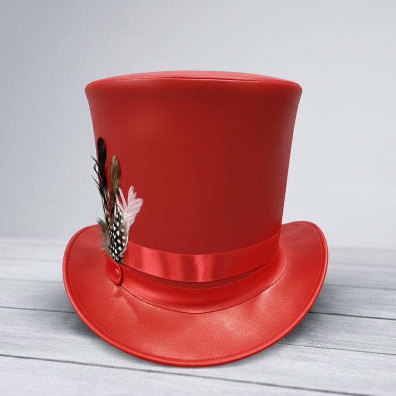 Puede incluir: Un sombrero de copa rojo brillante con ala ancha y cinta de raso. El sombrero est&aacute; adornado con un grupo de plumas decorativas en tonos negros, marrones y blancos. Un accesorio cl&aacute;sico.
