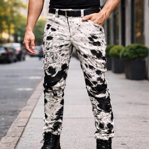 May include: White and black patterned jeans with a black belt and black boots. The jeans have a unique spotted design, and the boots are lace-up. The person is wearing a black t-shirt.