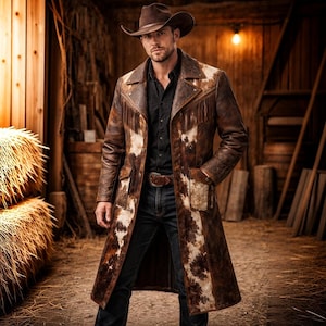 Puede incluir: Un abrigo largo de cuero marrón con un estampado de piel de vaca y flecos. El abrigo tiene un cuello con solapas, bolsillos y un cinturón. La persona lleva un sombrero de vaquero y una camisa negra.