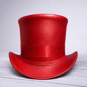 May include: A vibrant red top hat with a matching satin band. The hat has a classic tall crown and a slightly curved brim. The hat is made of a smooth, possibly leather-like material.