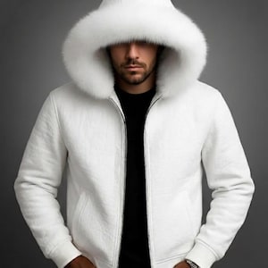 Puede incluir: Chaqueta blanca con capucha y capucha forrada de piel. La chaqueta tiene cierre de cremallera y bolsillos laterales. La persona de la imagen lleva una camiseta negra y vaqueros azules. La chaqueta es una prenda de abrigo de invierno.