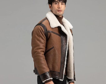 Puede incluir: Chaqueta de borrego marrón con forro y cuello de borrego color crema. La chaqueta presenta detalles de cuero marrón oscuro en los hombros, las mangas y los bolsillos. Estilo aviador clásico.