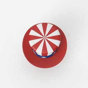 以下が含まれることがあります： 円形のつばが付いた赤いシルクハット。帽子の上面には、中央から放射状に広がる赤と白のストライプがあります。白い星が付いた青いバンドが帽子の底を囲んでいます。