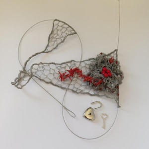 May include: A unique wire art piece featuring a gray, openwork design with red accents and a cluster of red berries. A silver heart-shaped lock and key are also included, creating a romantic theme.