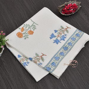 May include: White cotton towel with a floral pattern in orange and blue. The towel features a repeating floral border and is folded. The design includes the text "Block of Jaipur".