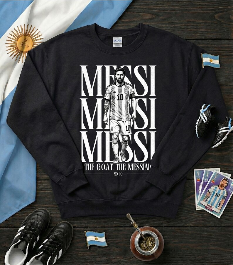 May include: Black sweatshirt with a graphic of a soccer player, with the name "MESSI" in white. The player is wearing a light blue and white jersey with the number 10. The text "THE G.O.A.T. THE MESSIAP" is below the image.