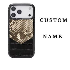 以下が含まれることがあります： ベージュと黒のヘビ柄の携帯電話ケース。黒いクロコダイル柄のベースが付いています。「CUSTOM NAME」の文字が側面に印刷されています。