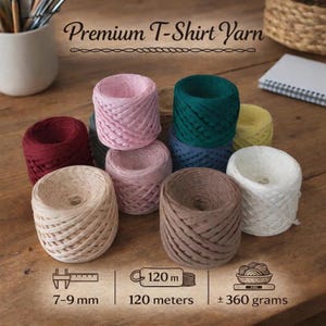 以下が含まれることがあります： ピンク、緑、ベージュなど、さまざまな色合いのカラフルなTシャツヤーンの糸巻きが木製の表面に配置されています。画像には「Premium T-Shirt Yarn」というテキストが含まれています。糸のサイズは7〜9mm、120メートルで、重さは約360グラムです。