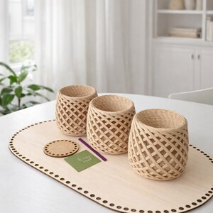 May include: Three woven, cylindrical baskets with a lattice design sit on a light wood oval base. A small coaster, a green card with text, and a purple stick are also on the base. The baskets are beige.