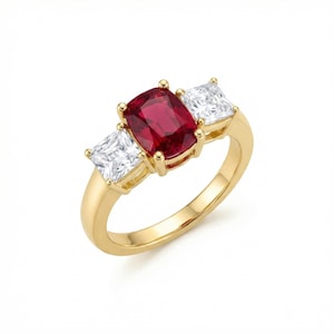 Op de afbeelding: Een gouden ring met een grote, rechthoekige, dieprode edelsteen geflankeerd door twee vierkante, heldere edelstenen. De ring heeft een gepolijste gouden band en de edelstenen zijn gezet in een klassiek ontwerp met drie stenen.