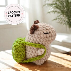 May include: A crocheted mushroom-shaped plush toy in beige, with brown accents and a green backpack. The toy has closed eyes and is made with a thick, textured yarn. A circular graphic reads "CROCHET PATTERN".