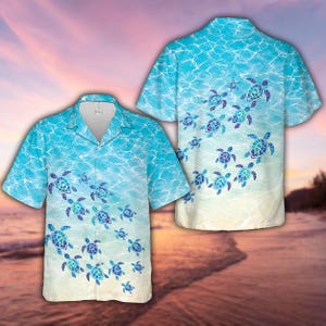 May include: A short-sleeved button-down shirt featuring a light blue water surface pattern with ripples and a repeating print of sea turtles in shades of blue and green. The shirt has a notched collar and a gradient design fading to a sandy beige colour.