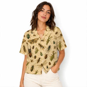 May include: A short-sleeved button-down shirt in a light beige color featuring an all-over print of various insects, including beetles, dragonflies, moths, and praying mantises in shades of brown, green, and black with a notched collar.
