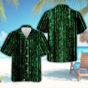 May include: A short-sleeved button-down shirt featuring a black background with a vertical digital rain pattern in bright green. The design consists of cascading alphanumeric characters and symbols, mimicking a computer code aesthetic throughout.