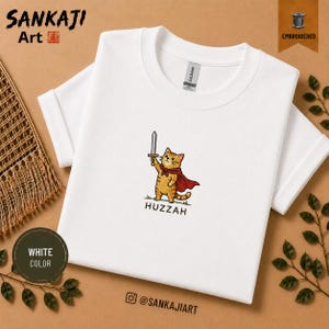 Op de afbeelding: Een wit T-shirt met korte mouwen en een geborduurde afbeelding van een oranje cyperse kat met een rode cape die een zilveren zwaard vasthoudt. Onder de kat staat de tekst HUZZAH in zwarte hoofdletters. Het T-shirt heeft een ronde hals.