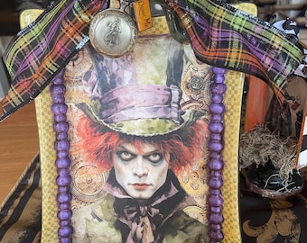 Könnte beinhalten: Ein dekorativer quadratischer Teller mit dem Hutmacher aus Alice im Wunderland. Der Teller hat einen gelben Rand, eine lila Perlenverzierung und einen grünen Griff. Ein kariertes Band und eine Taschenuhr ergänzen das skurrile Design.