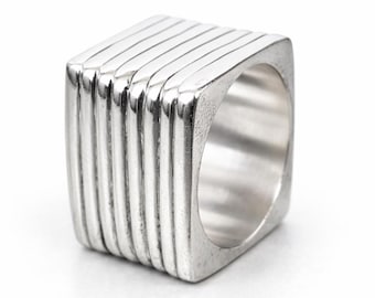 Anillo cuadrado brutalista de plata de ley maciza, con banda geométrica acanalada de varias capas.