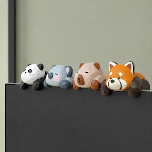 Puede incluir: Cuatro figuras de animales de madera: un panda, un koala, un oso y un panda rojo. El panda es blanco y negro, el koala es gris y rosa, el oso es marrón claro y el panda rojo es naranja y blanco. Cada figura está sobre una superficie negra.