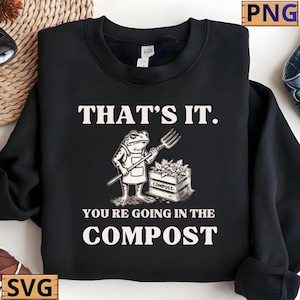 Op de afbeelding: Zwarte sweatshirt met de tekst "THAT'S IT. YOU'RE GOING IN THE COMPOST." Een cartoon kikker met een schort houdt een tuinvork vast naast een compostbak. De tekst en afbeelding zijn wit.