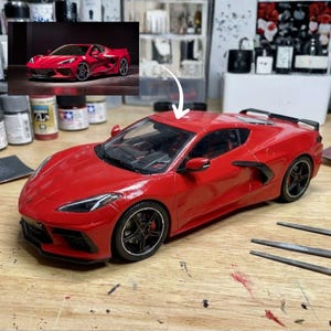 Könnte beinhalten: Ein rotes Modellauto eines Chevrolet Corvette Sportwagens mit schwarzen Rädern, einem schwarzen Heckspoiler und einem detaillierten Innenraum. Ein kleines eingefügtes Foto zeigt dasselbe rote Auto aus der Seitenansicht, verbunden durch einen weißen Pfeil.