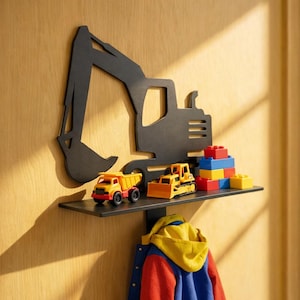 Peut inclure: Étagère murale noire en forme de pelle mécanique avec une étagère contenant des camions jouets et des blocs de construction. Une veste colorée est suspendue en dessous. L'étagère est fixée sur un mur en bois clair.