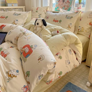 Pode incluir: Conjunto de roupa de cama creme com uma estampa de desenho animado caprichosa com carros, árvores e personagens de animais. O conjunto inclui uma capa de edredom, fronhas e um brinquedo de pelúcia de cachorro. O esquema de cores geral é suave e convidativo.