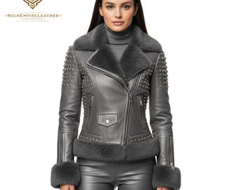 May include: A gray leather jacket with a shearling collar and cuffs. The jacket features a zipper closure, studded accents on the shoulders and sleeves, and a small pocket on the chest. The logo "NOIREMPIRELEATHER" is visible in the upper left corner.
