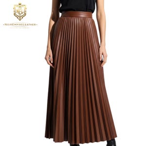May include: A long, pleated brown skirt with a wide waistband. The skirt is made of a leather-like material and falls to the ankles. The image also includes the logo of Noir Empire Leather.
