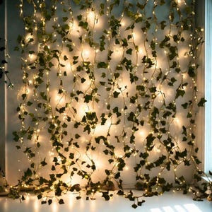 Pode incluir: Uma corda decorativa de luzes LED brancas quentes entrelaçada com videiras de hera artificial. As folhas verdes e as pequenas luzes criam um brilho suave e ambiente, ideal para decoração de casa ou estilo de eventos.