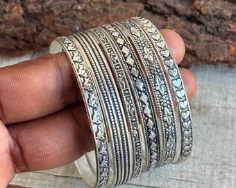 Peut inclure: Ensemble de bracelets en argent ornés de motifs floraux et géométriques détaillés. Les bracelets sont empilés, présentant des motifs de feuilles, de fleurs et de cœurs. Les bracelets en argent ont une finition polie, reflétant la lumière.
