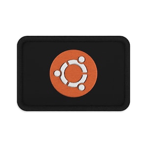 Puede incluir: Un parche rectangular bordado en negro que presenta un círculo naranja centrado. Dentro del círculo naranja hay un logotipo blanco estilizado de Ubuntu que consiste en tres formas circulares interconectadas con puntos blancos.