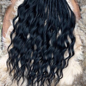 May include: Black wavy hair extensions, with a combination of dreadlocks and loose curls. The hair is a deep black color, and the texture appears soft and flowing. The extensions are displayed on a wooden surface with a natural, earthy background.