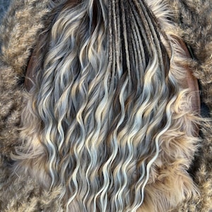 Peut inclure: Un ensemble de dreadlocks dans les tons marron, gris et blond, avec des extrémités ondulées. Les dreadlocks sont attachées en haut avec une ficelle. Le fond présente des herbes ornementales séchées.