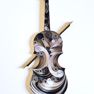 May include: A paper quilling violin in shades of black, white, and grey. The instrument's body and neck are decorated with spiral patterns. A black bow is positioned across the violin, showcasing the craftsmanship.