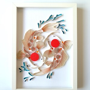 Könnte beinhalten: Ein gerahmtes Papierkunstwerk mit zwei Koi-Karpfen in einer Yin-Yang-Komposition. Die Fische sind weiß mit orangefarbenen und beigen Details, roten Flecken und blauen Wasserakzenten. Das Kunstwerk befindet sich vor einem weißen Hintergrund in einem weißen Rahmen.