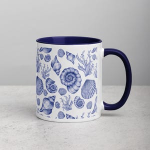 Puede incluir: Taza de cerámica blanca con interior y asa azules. El exterior presenta un patrón de conchas marinas y corales azules. La taza está diseñada para bebidas frías o calientes.