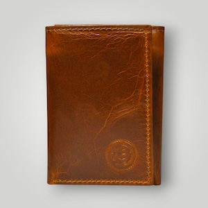May include: A tri-fold leather wallet in a warm brown hue. The wallet features a textured surface and visible stitching along the edges. A circular emblem is embossed on the front. This accessory is designed for carrying cards and cash.