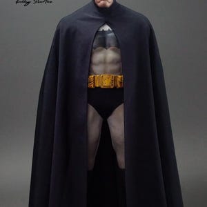 Può includere: Action figure di Batman con mantello, cappuccio e slip neri. La figura ha una cintura di utilità gialla e un fisico muscoloso. La figura è in piedi davanti a uno sfondo grigio. La figura è di Kelly Studio.