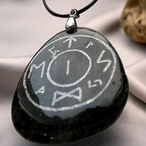 Peut inclure: Pendentif en pierre noire avec une bélière en métal argenté et un cordon noir. La pierre présente des symboles gravés en blanc et un chiffre 1 central dans un cercle. Le pendentif est lisse et poli.