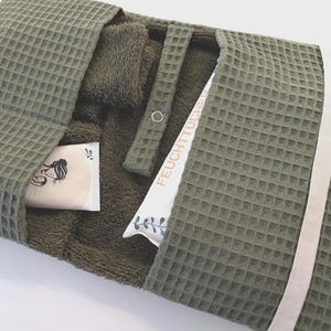 Könnte beinhalten: Ein olivgrüner Organizer aus Waffelstoff mit Druckknopfverschluss, weißem Band und zwei Innentaschen. Eine Tasche enthält eine Packung mit der Aufschrift FEUCHTTÜCHER, die andere einen kleinen Gegenstand mit einer schwarzen Strichzeichnung.