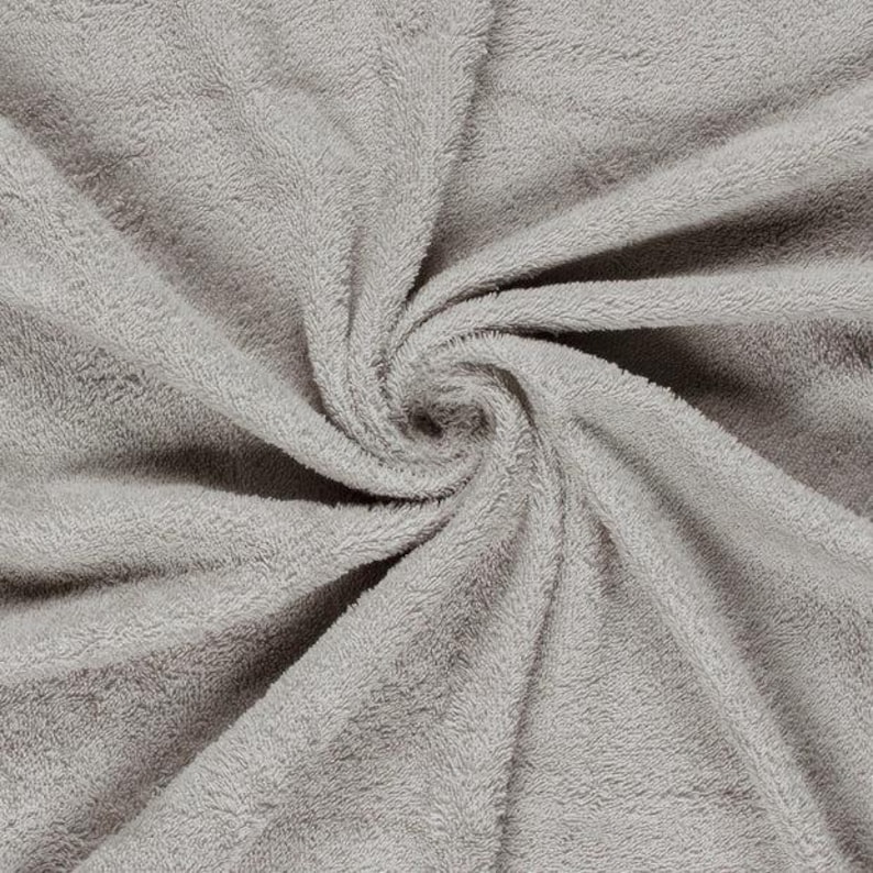 May include: A light gray towel featuring a dense, soft, and plush terry cloth texture. The fabric is arranged in a central spiral pattern, highlighting the consistent pile and the uniform neutral color across the entire surface of the textile.