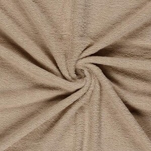 May include: A solid light brown fabric with a soft, plush, and fuzzy texture. The material is gathered in the center, creating radiating folds and ripples that highlight the dense, short pile of the textile surface across the entire frame.