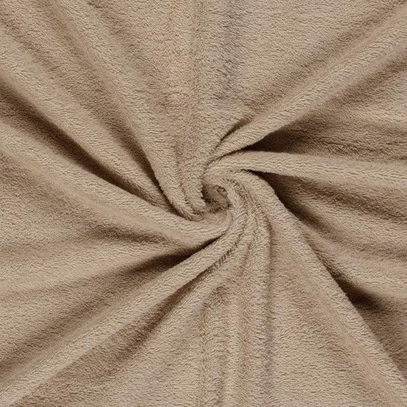 May include: A solid light brown fabric with a soft, plush, and fuzzy texture. The material is gathered in the center, creating radiating folds and ripples that highlight the dense, short pile of the textile surface across the entire frame.