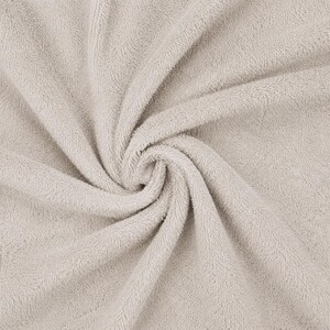 May include: A light beige towel featuring a dense, soft, and absorbent terry cloth texture. The fabric is arranged in a swirling, gathered pattern that highlights the looped pile construction and the consistent neutral color throughout the material.