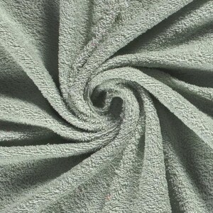 May include: A sage green towel featuring a dense, looped terry cloth texture. The fabric is arranged in a swirling, spiral pattern that radiates from the center, highlighting the soft, absorbent material and the consistent light green color.