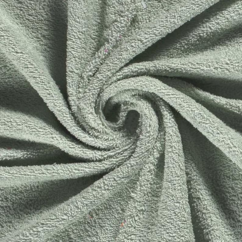 May include: A sage green towel featuring a dense, looped terry cloth texture. The fabric is arranged in a swirling, spiral pattern that radiates from the center, highlighting the soft, absorbent material and the consistent light green color.