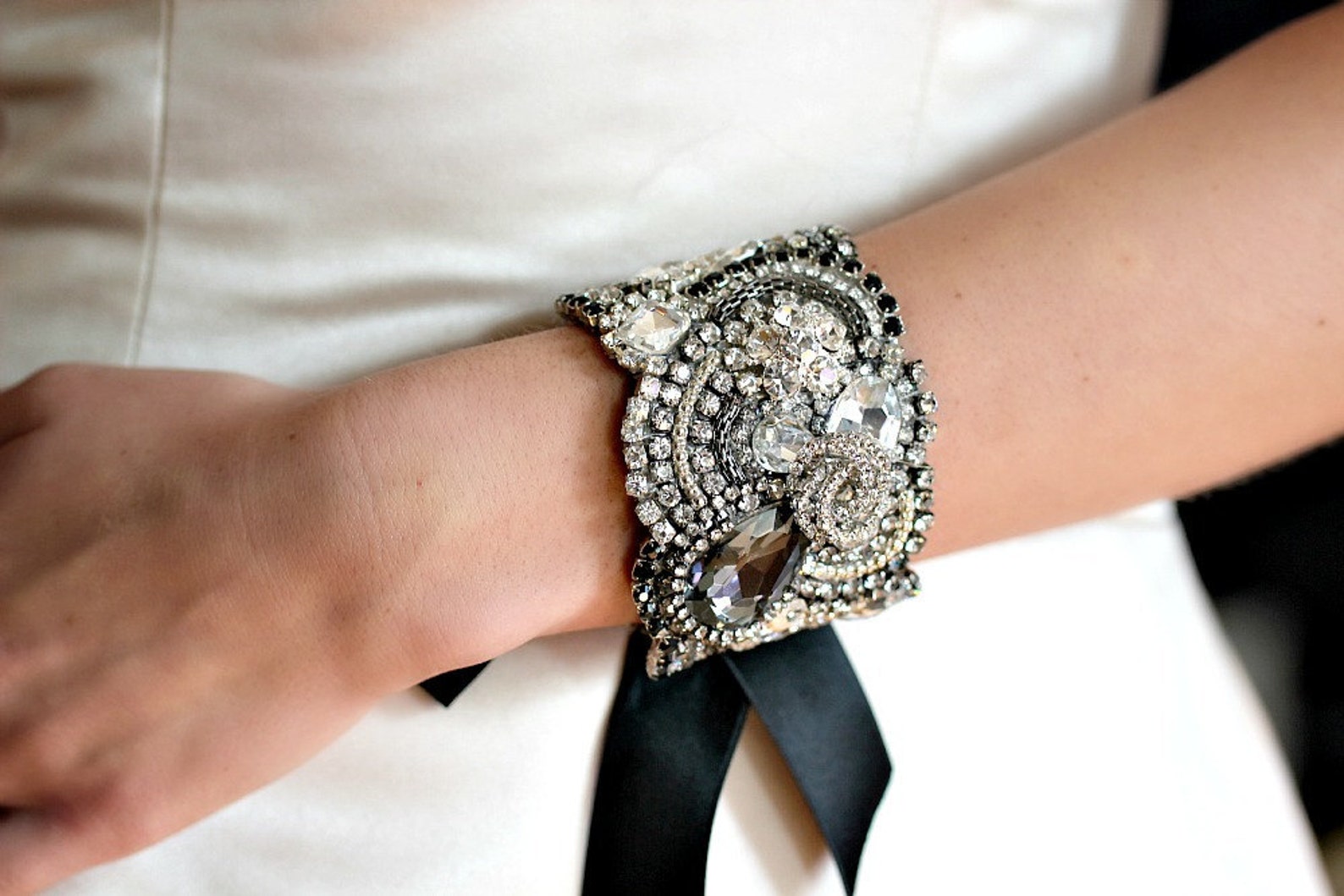 Black and clear crystal bridal cuff worn over satin dress, tied with black ribbon