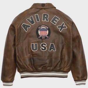 May include: Brown leather jacket with the word "AVIREX" arched across the shoulders in white block letters. Below is a circular patch with the American flag and the words "ALL AMERICANS ESTABLISHED 1975". The word "USA" is below the patch.
