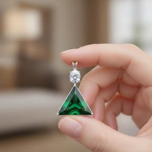 May include: A silver pendant featuring a triangular, emerald-green gemstone with a brilliant-cut, round, clear stone above it. The pendant is held between fingers, showcasing its design and color.
